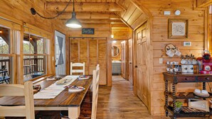 Ein Holzblockhaus-Interieur mit Essbereich, Holzwänden und einer durchgehenden Tür erkennbaren Küche.