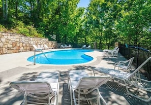 Una piscina con sillones de descanso y un muro de piedra.