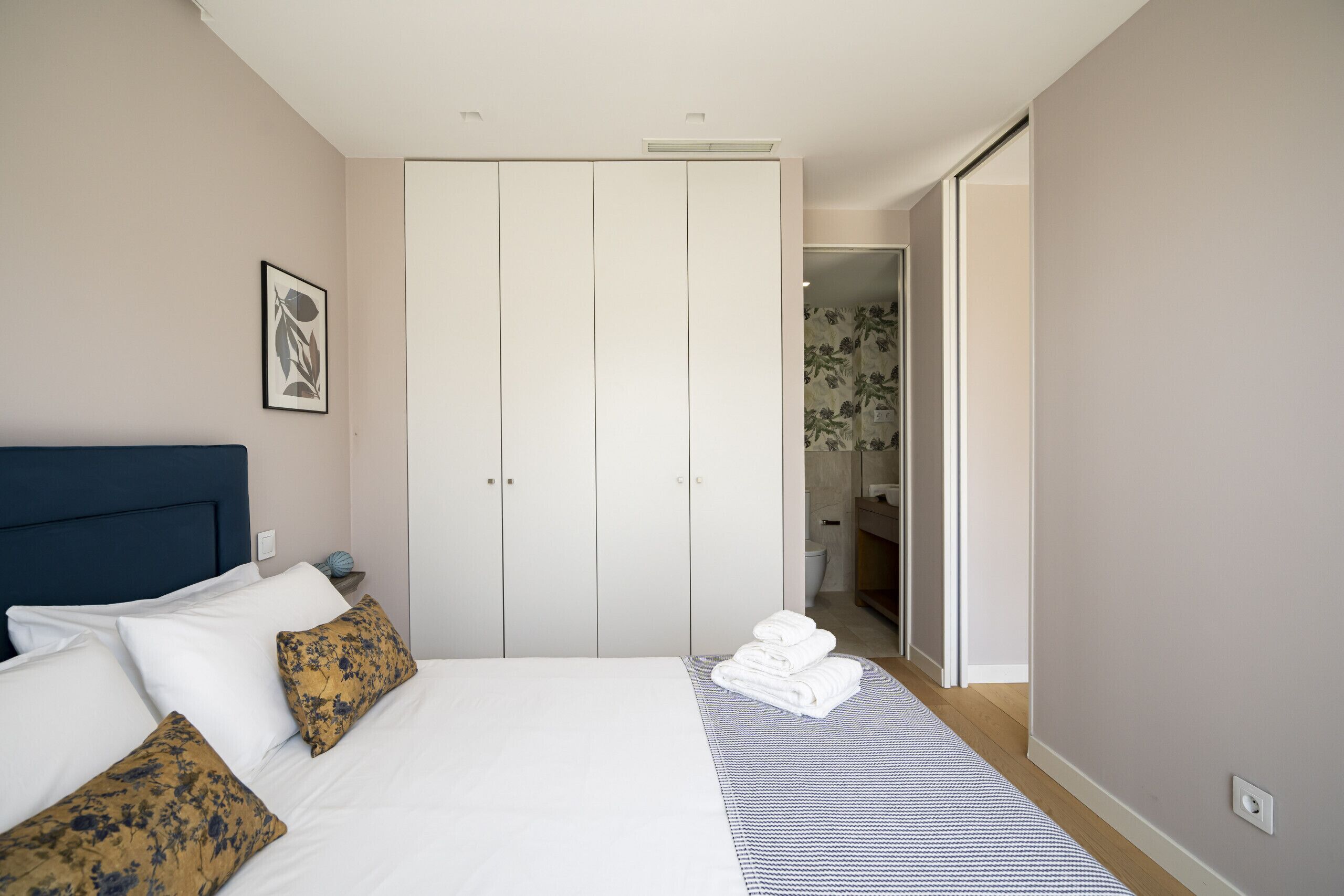A neatly arranged bedroom with a large bed, a wardrobe, and a bathroom visible through an open door.
