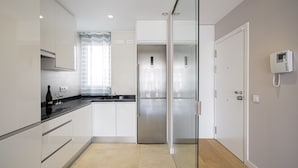 A modern kitchen with white cabinets, a stainless steel refrigerator, and a glass door leading to another room. - PALACIO REAL - MADRID, 2HH, 2 BAÑOS, 6 PAX (Madrid)