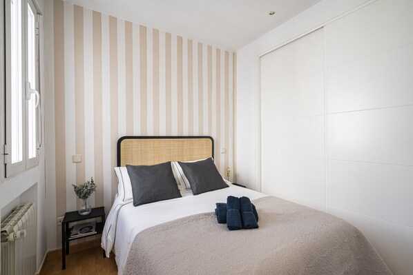 A neatly arranged bedroom with a bed, a nightstand, a radiator, and a window.