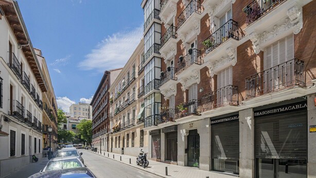 A street view of a building with multiple balconies, a parked motorcycle, and storefronts with signage. - Apartamento Santa Engracia-Bilbao (Madrid)