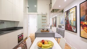 A modern kitchen with white cabinets, a grey countertop, and a fruit bowl on the dining table. - Apartamento Santa Engracia-Bilbao (Madrid)