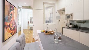A modern kitchen with white cabinets, a black countertop, and a dining area with a gray sofa. - Apartamento Santa Engracia-Bilbao (Madrid)