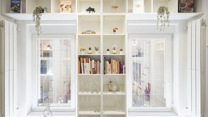 A white interior with a bookshelf filled with books and glassware, and a window with a view of the outside. - Apartamento Santa Engracia-Bilbao (Madrid)