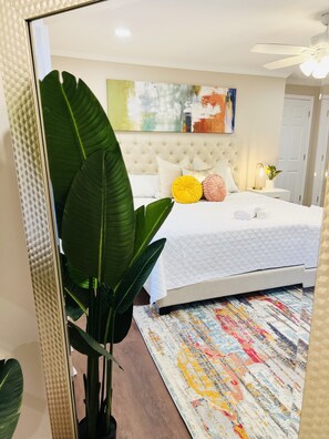 Een slaapkamer met een bed, nachtkastje, plafondventilator en een grote plant.