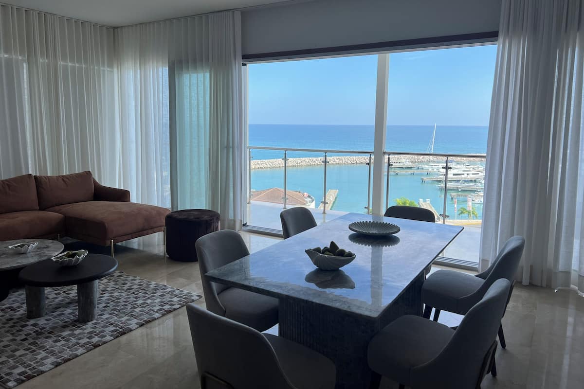 Een moderne woonkamer met een groot raam met uitzicht op een jachthaven en de zee.
