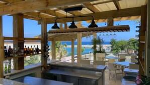 Zona de bar al aire libre con vistas al mar, pérgola de madera y asientos.