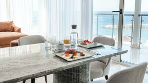 Un comedor con una mesa lista para el desayuno, vista al mar y un balcón con barandilla de vidrio.