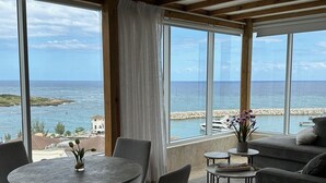 Una habitación con un amplio ventanal con vista al mar, una mesa redonda con sillas y un sofá.