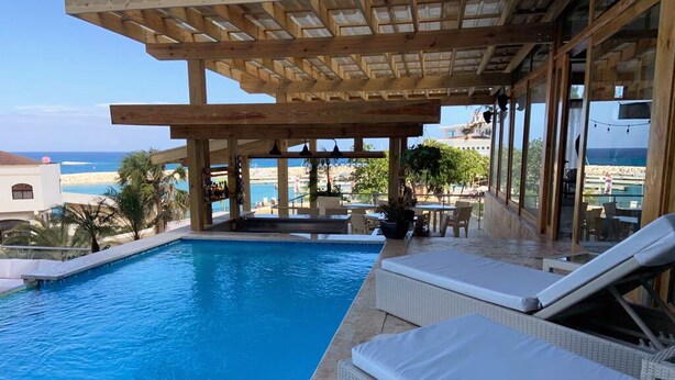 Zona de piscina con sillones de descanso y una pérgola con vistas al mar.