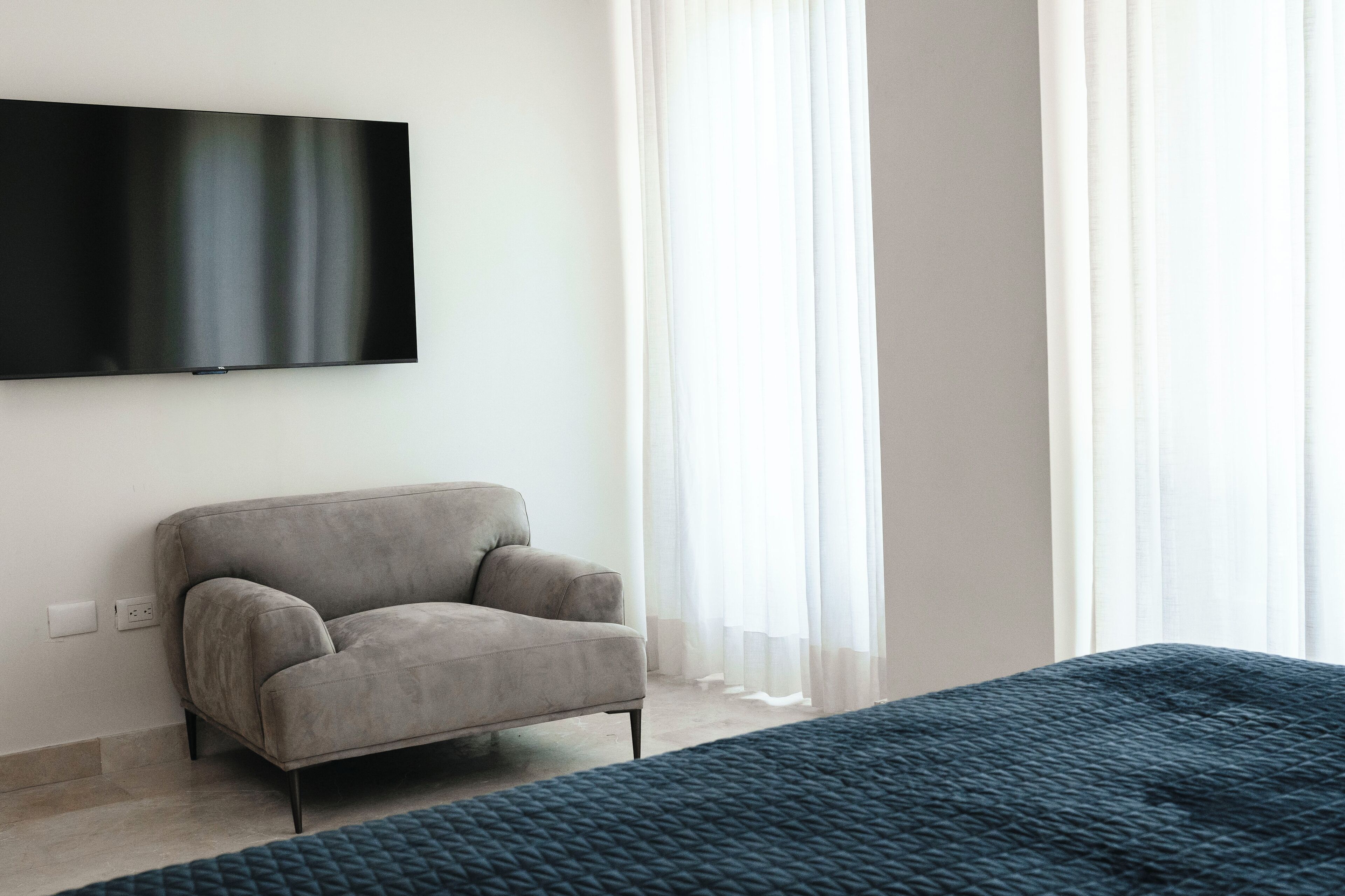 Ein modernes Wohnzimmer mit einem an der Wand befestigten Flachbildfernseher, einem grauen Sofa und transparenten Vorhängen.