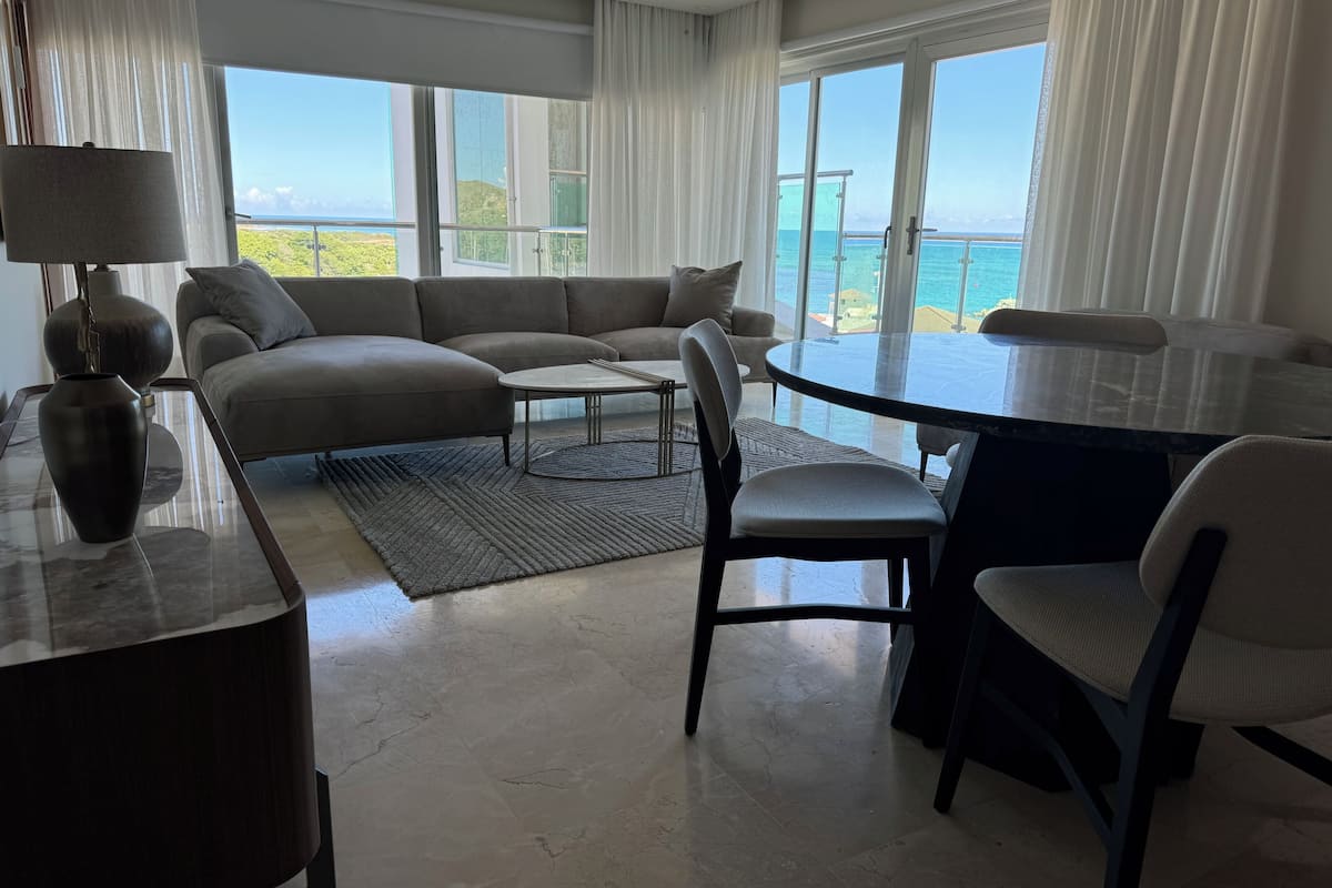 Een moderne woonkamer met een hoekbank, een glazen eettafel en uitzicht op zee.
