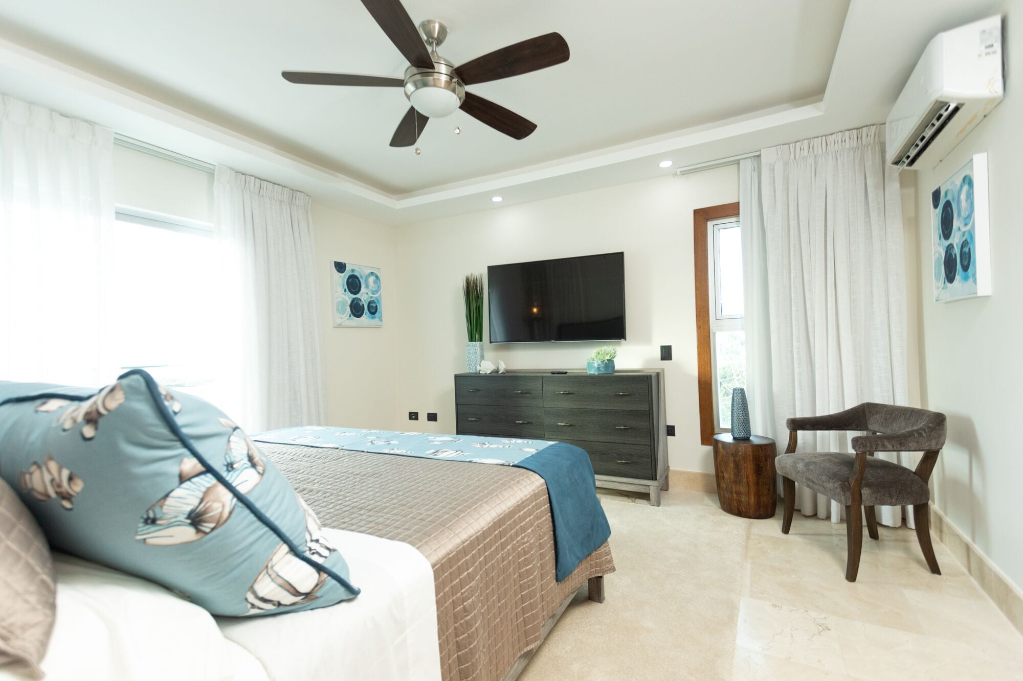 A bedroom with a bed, a chair, a dresser, a TV, and a ceiling fan.