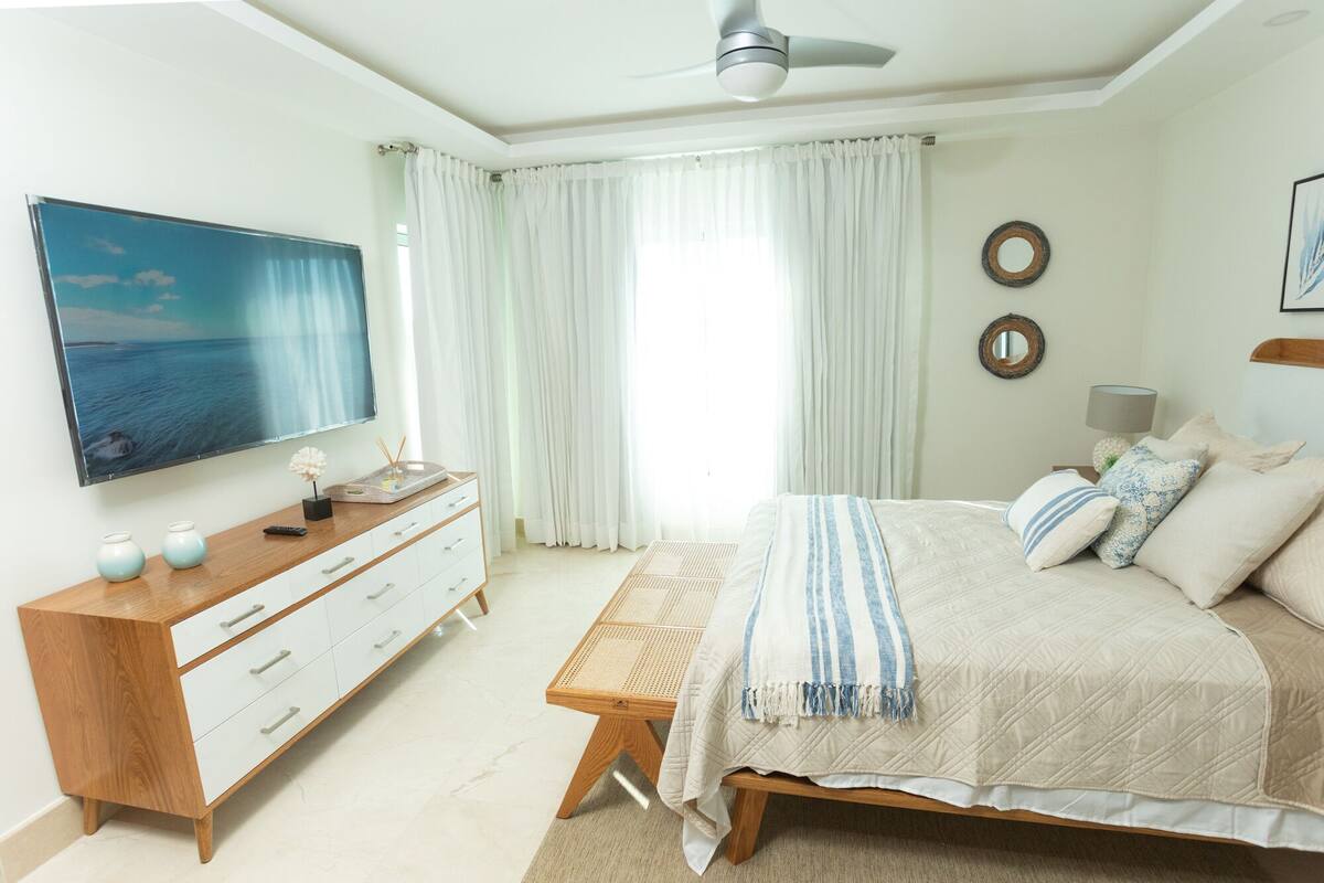Een slaapkamer met een bed, een houten dressoir, een televisie en een plafondventilator.