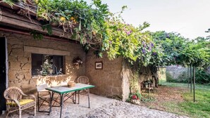 A rustic stone building with a stone patio, a table with chairs, and a garden with climbing plants and flowers. - The Borgo Renaissance Stable (Farnese)