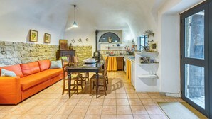 A cozy living room with a stone wall, a wooden dining table, and a bright orange sofa. - The Borgo Renaissance Stable (Farnese)