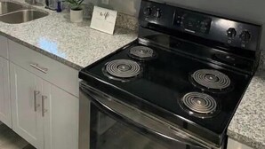 Een moderne keuken met witte kastjes, een roestvrijstalen magnetron, een zwart fornuis en een granieten aanrecht.