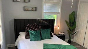Een slaapkamer met een bed, nachtkastje, raam en plafondventilator.