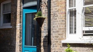 A blue door with a hanging plant, brick walls, and a window with shutters.