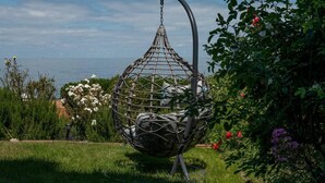 A garden with a hanging chair made of woven material, surrounded by various plants and flowers.