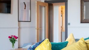 A modern living room with a yellow sofa, a framed picture on the wall, and a door leading to another room.