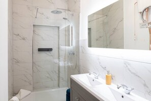 Un baño moderno con ducha de vidrio, un espejo grande y un lavamanos con dos senos.