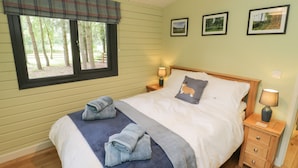 Une chambre à coucher comprenant un lit, deux tables de chevet, une fenêtre donnant sur des arbres et trois tableaux encadrés accrochés au mur.