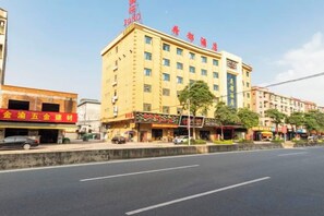 A multi-story hotel with a prominent sign, a street in front, and several storefronts. - Hedu Hotel (Dongguan Qiaotou) (Dongguan)