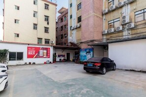 Un estacionamiento con un coche negro, un edificio de varios pisos y un anuncio rojo en la pared.