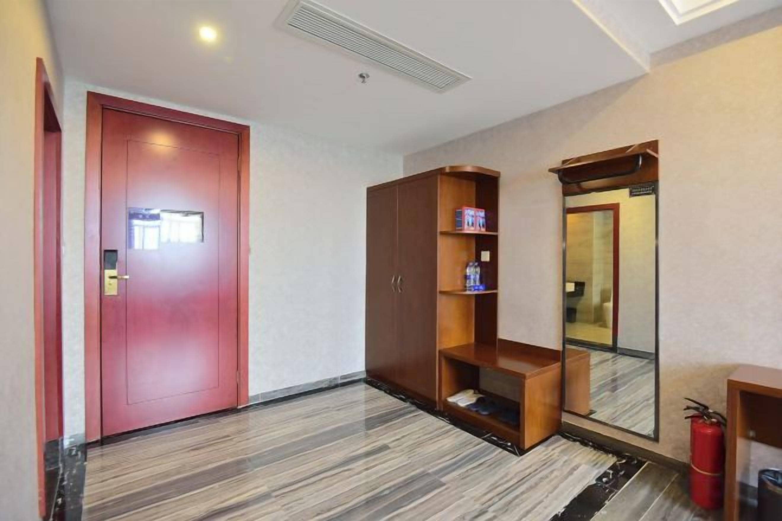 Corredor de hotel com uma porta vermelha, um guarda-roupa de madeira e um espelho.