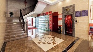 Un vestíbulo de hotel con piso de mármol, una escalera, un vitrina de vidrio y una puerta con la indicación "1F".