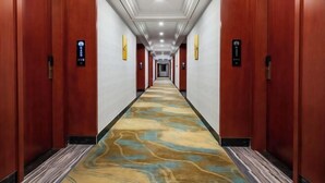 A hotel hallway with wooden doors, a patterned carpet, and a long corridor. - Hedu Hotel (Dongguan Qiaotou) (Dongguan)