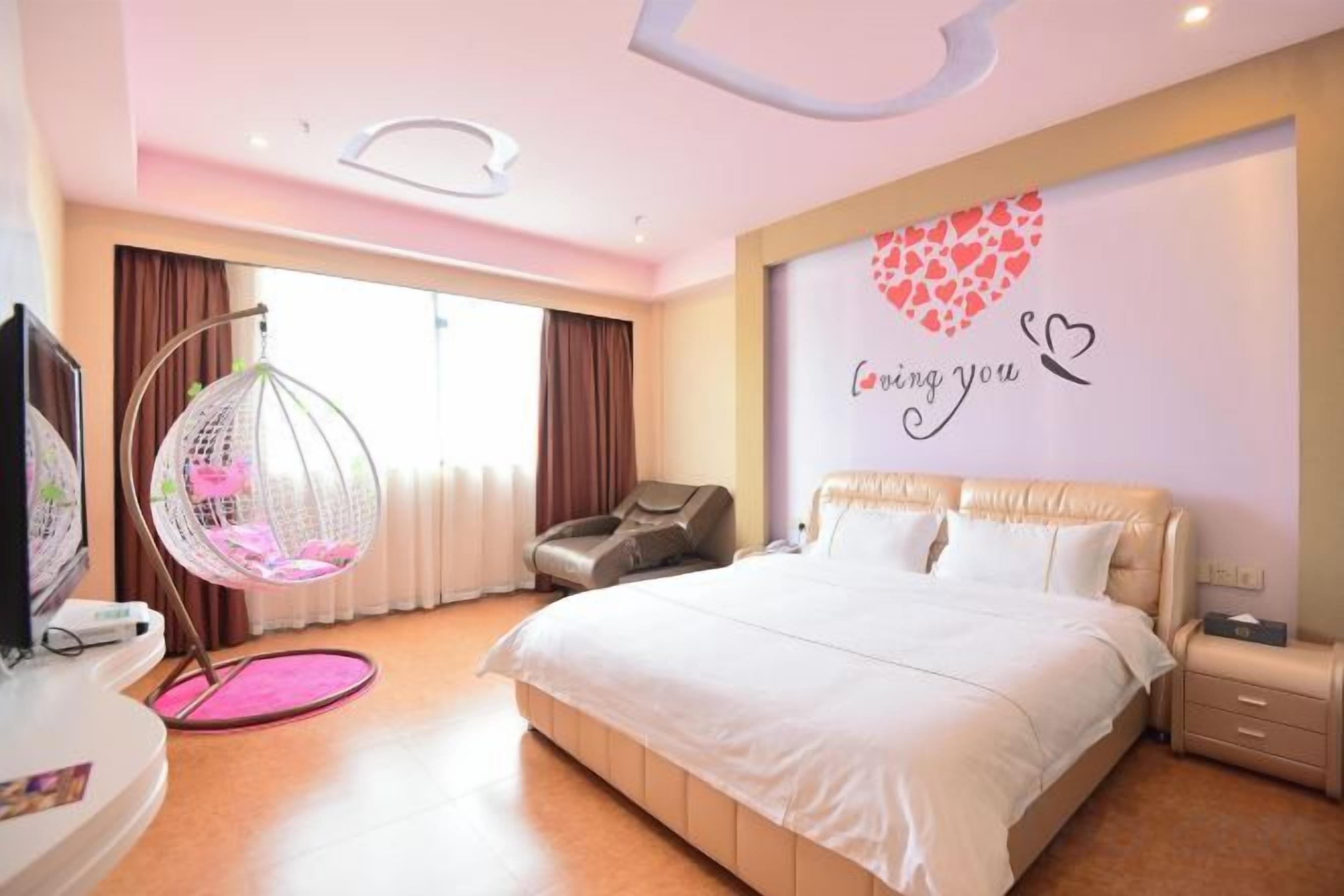 Een hotelkamer met een groot bed, een televisie, een hangstoel en een wand met een decoratie in de vorm van een hart.