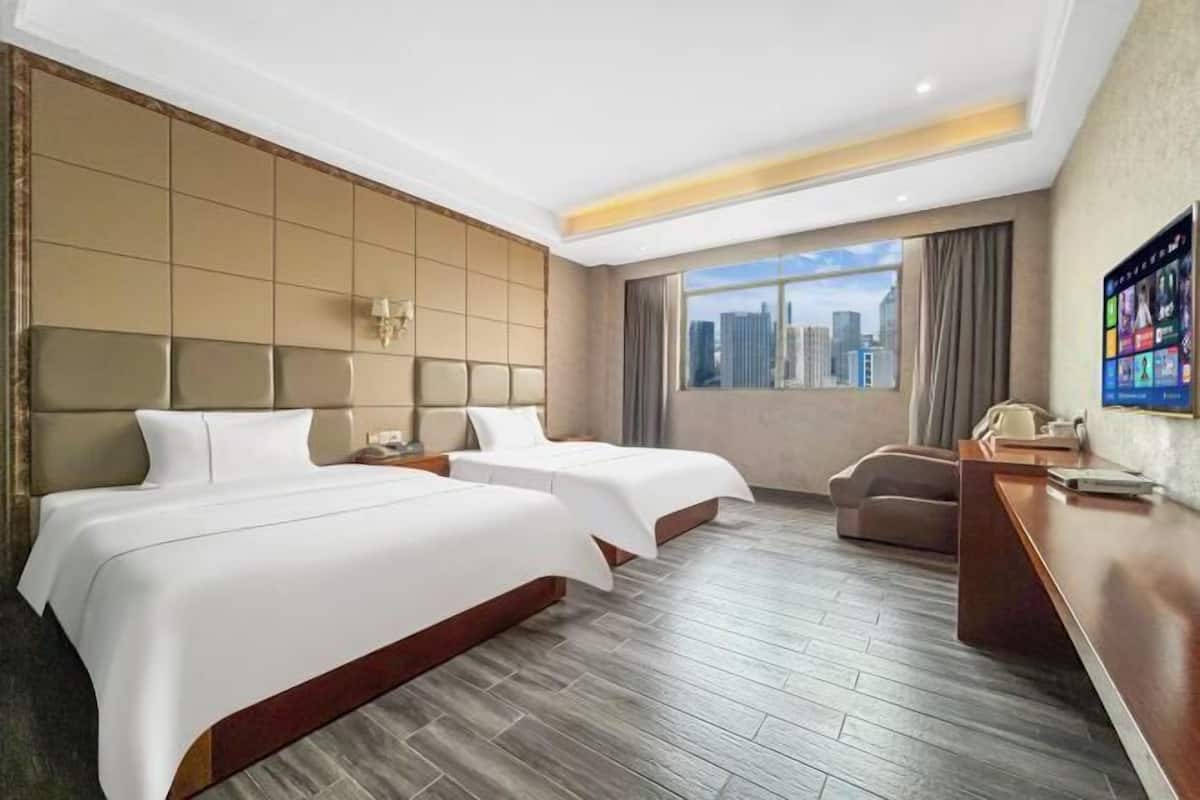 A hotel room with two beds, a desk, and a view of the cityscape.