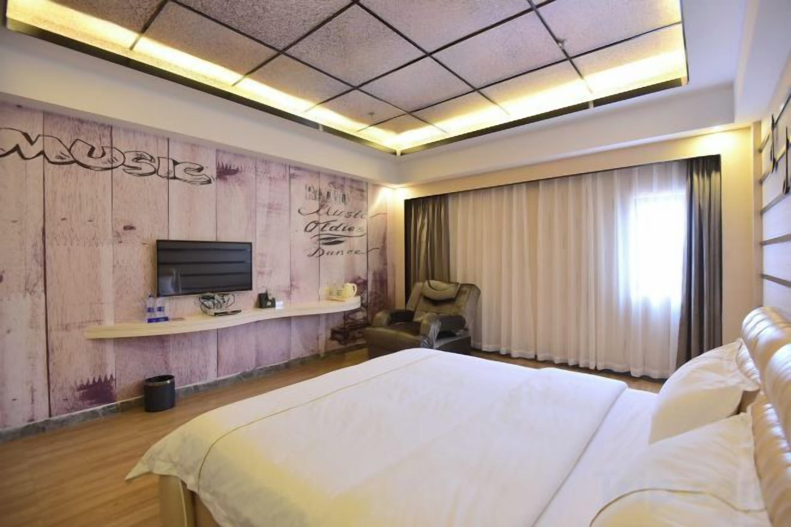 Una camera d'albergo con un letto grande, una TV a parete, un divano e una finestra con tende.