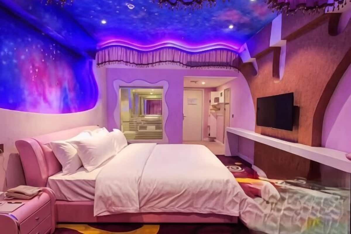 A bedroom with a bed, a vanity, and a television.