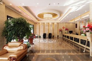 Un hall de hotel con una recepción, una planta en maceta grande, un sofá y una araña.
