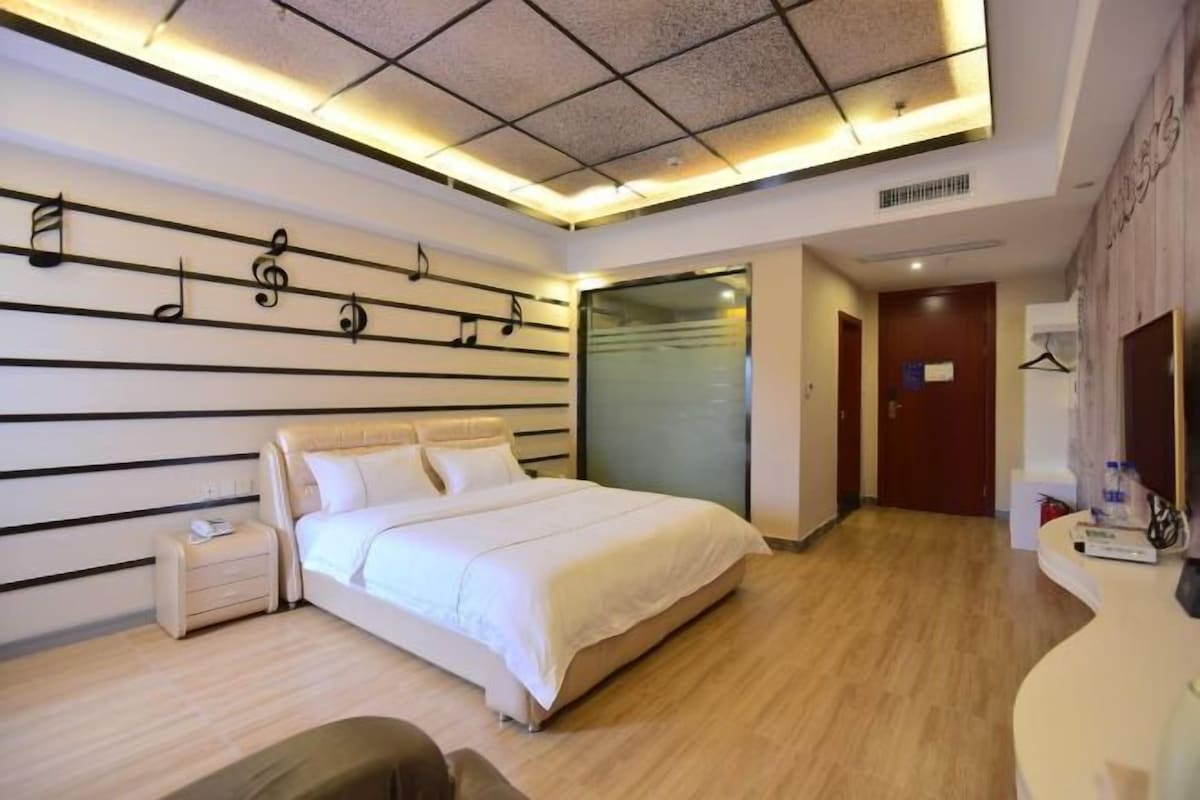 Una habitación de hotel moderna con una cama grande, una mesita de noche, un armario y un baño visible a través de una puerta de cristal.