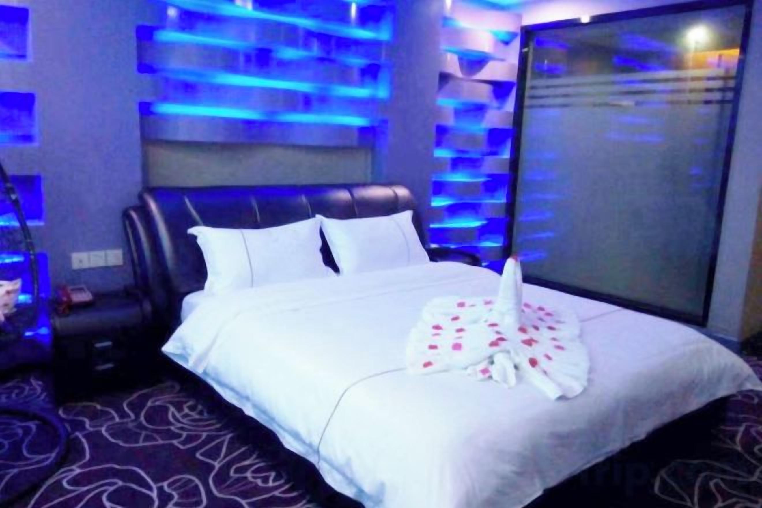 A hotel room with a bed, a headboard, a window, and a wall with a patterned design.