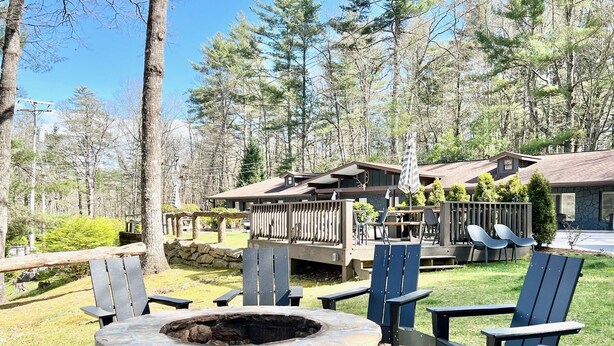 Kivistä rakennettu nuotiopaikka, jonka ympärillä on Adirondack-tyylisiä puutarhatuoleja, puinen terassi ja kivestä tehty rakennus, jonka julkisivu on myös kivestä.