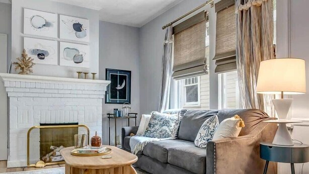 A living room with a fireplace, a grey sofa, a round coffee table, and a lamp. - Forth House - Butterfly Getaway in Historic SPR! (Jacksonville)