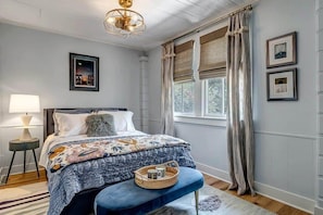 Une chambre à coucher avec un lit, une table de chevet, une lampe et une fenêtre avec des rideaux.