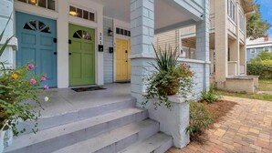 A two-story house with a porch, three doors in blue, green, and yellow, and a brick pathway leading to the entrance. - Forth House - Butterfly Getaway in Historic SPR! (Jacksonville)