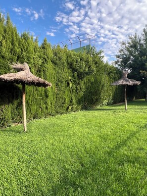 Una zona verda amb dues sobreades de palla i un fons de vegetació abundant.