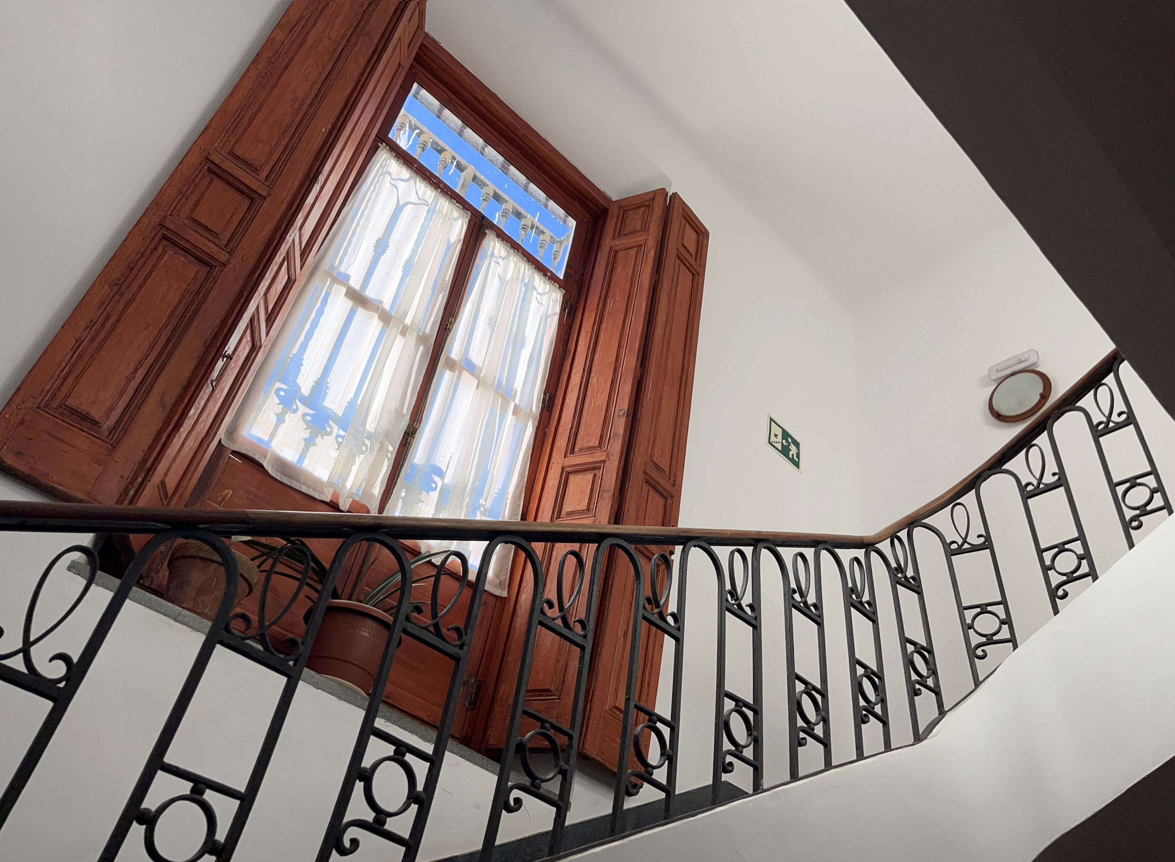 A staircase with a handrail, wooden doors, and a window with curtains.