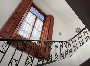 Una escala amb barana, portes de fusta i una finestra amb cortines.