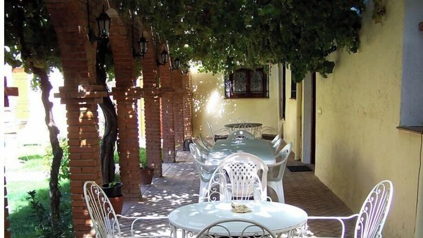 An outdoor patio with white metal tables and chairs, brick pillars, and hanging lanterns. - Elegant Manor House near Alcalá del Jucar with Piano. (Pozo-Lorente)