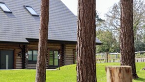 A log cabin with a sloped roof, large windows, and a grassy yard with tall trees. - Ghyll Park Farm (Heathfield)