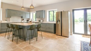A spacious kitchen with a central island, bar stools, a stainless steel refrigerator, and a large window providing natural light. - Ghyll Park Farm (Heathfield)